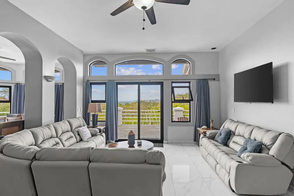 Living room with two grey sectional sofas, marble floors, and arched glass doors opening to the ocean-view terrace