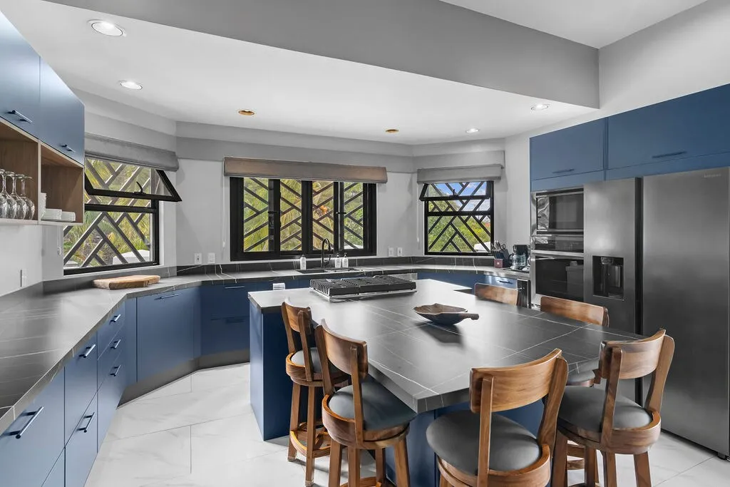 Fully equipped kitchen with navy cabinets, large stone island with bar seating, and wraparound windows